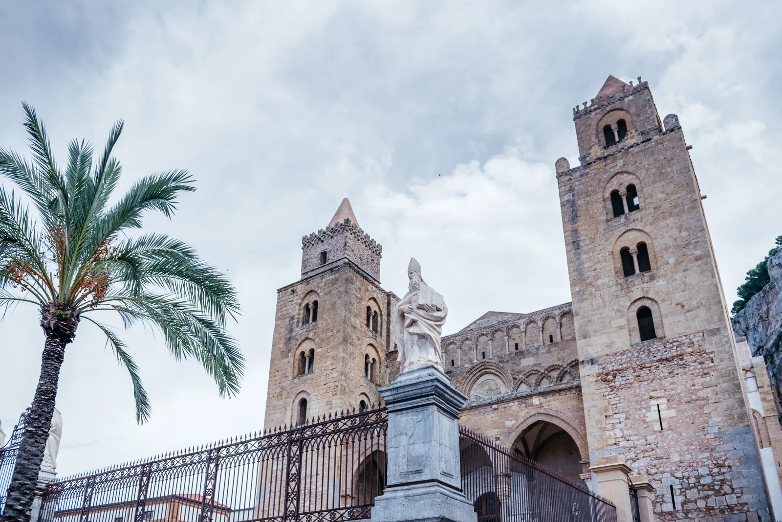 The twin Norman towers of Cefalù cathedral with a palm in the foreground