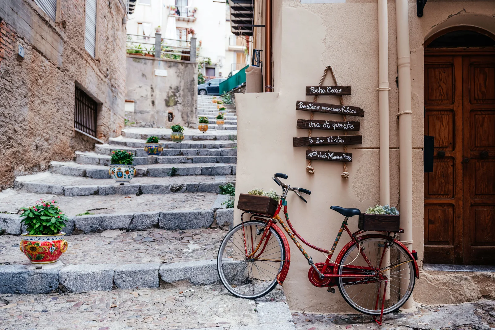 A red bicycle propped beside stone steps in a Cefalù lane