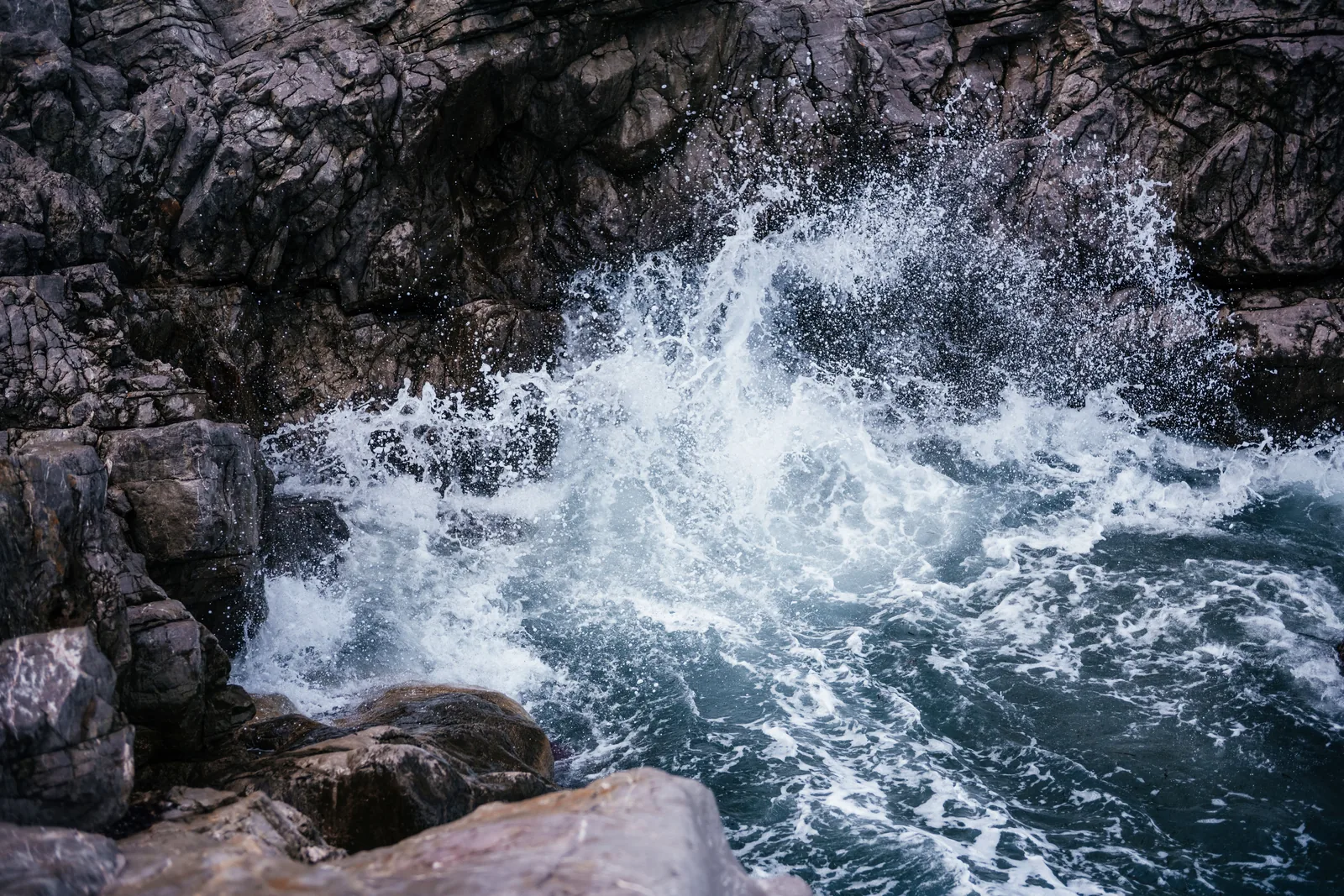 Waves breaking white against dark rocks on the Cefalù shore