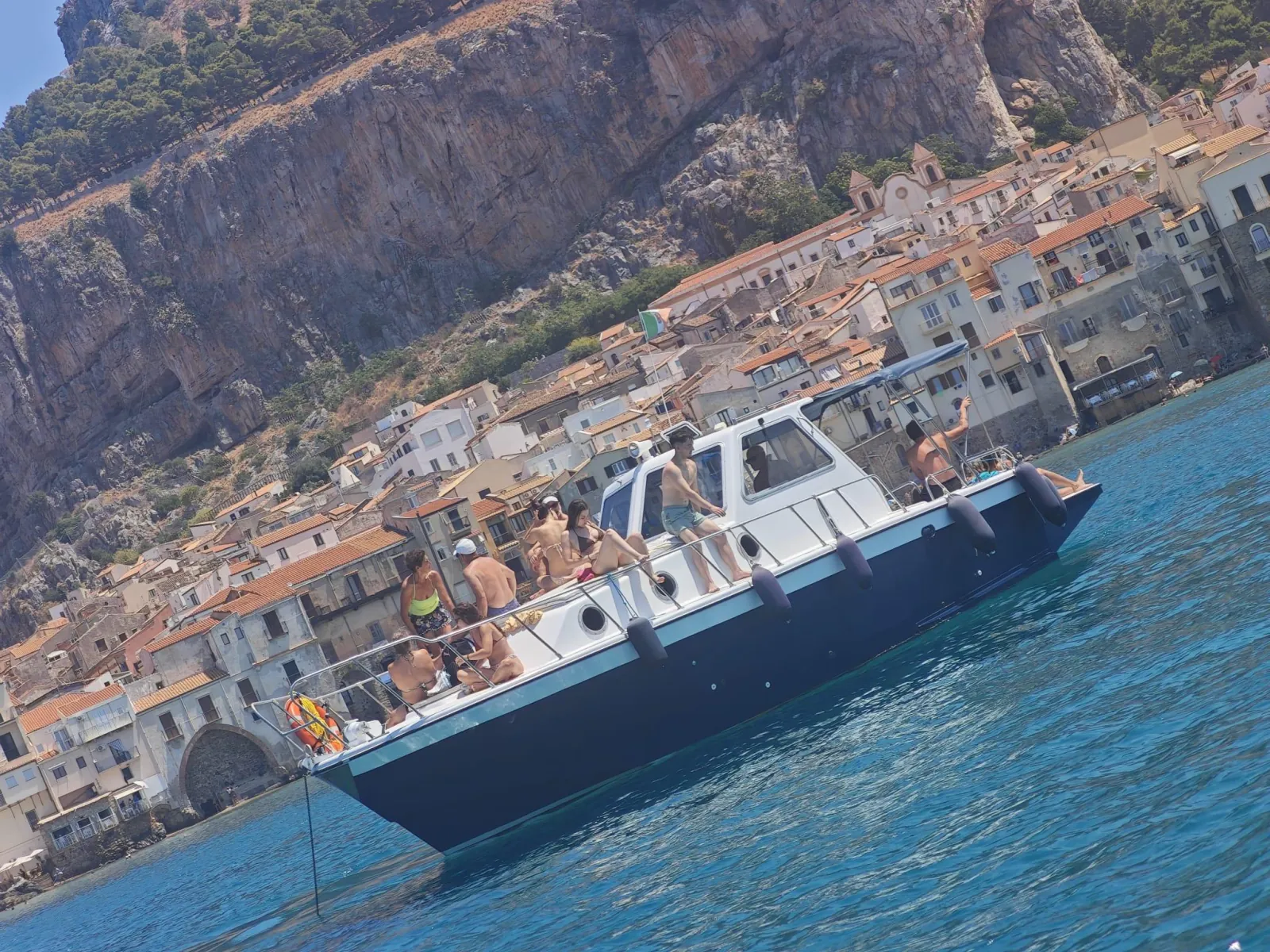 The boat close in below the cliffs of La Rocca, with the old town stacked behind it