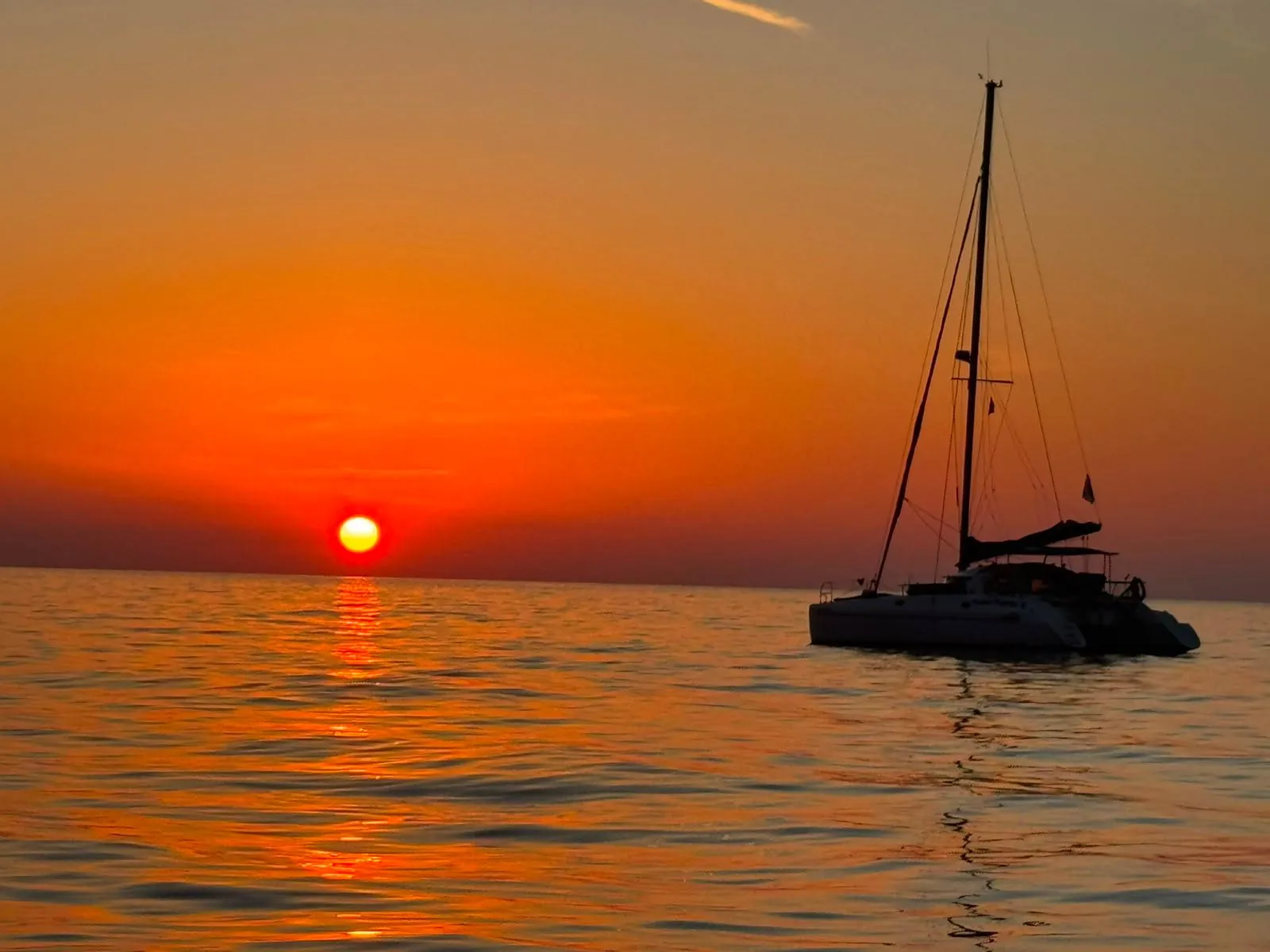 The sun dropping into the sea off Cefalù, with a yacht in silhouette on the horizon