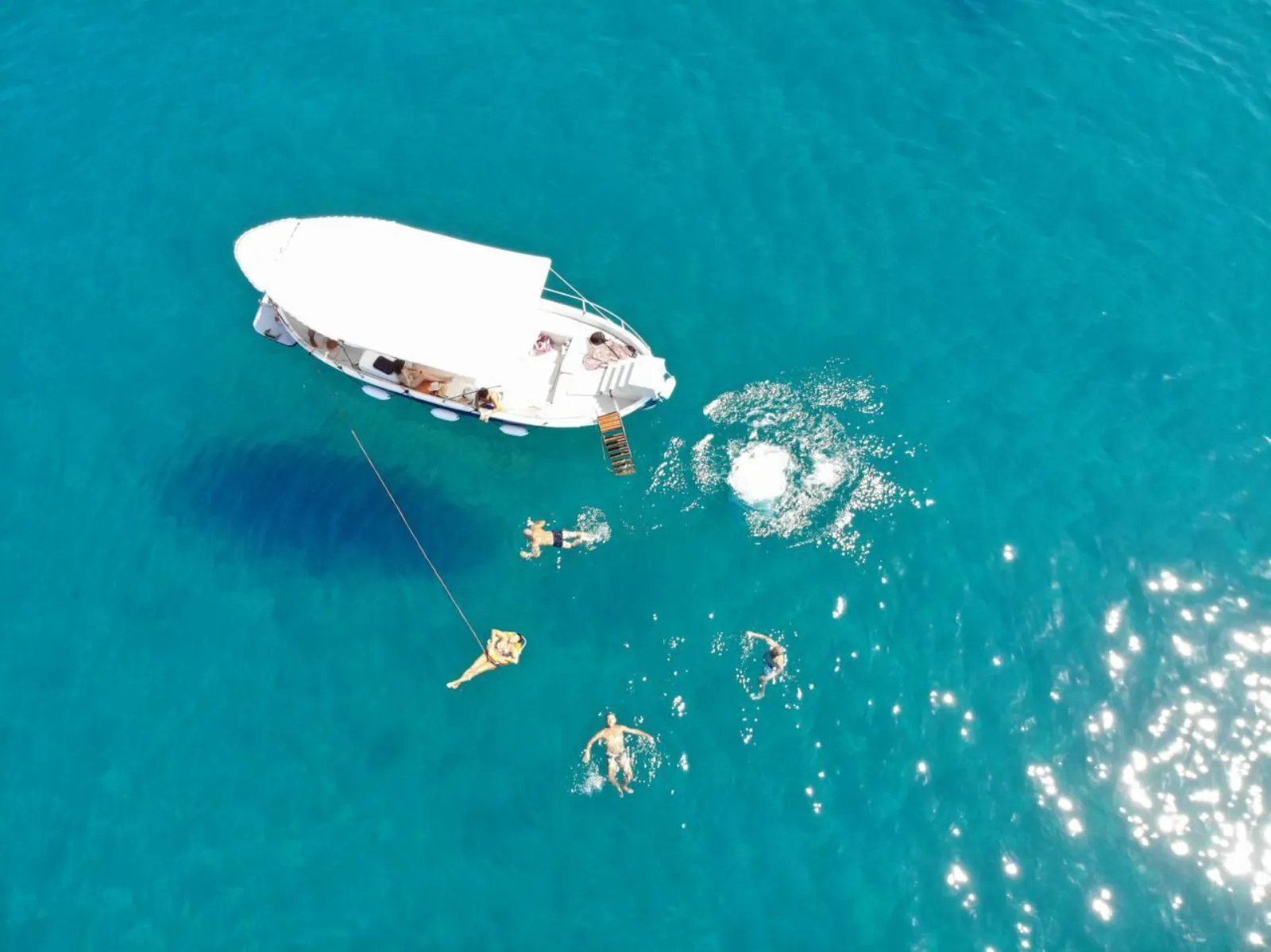 Closer aerial of the swimming stop, swimmers alongside the boat in clear water