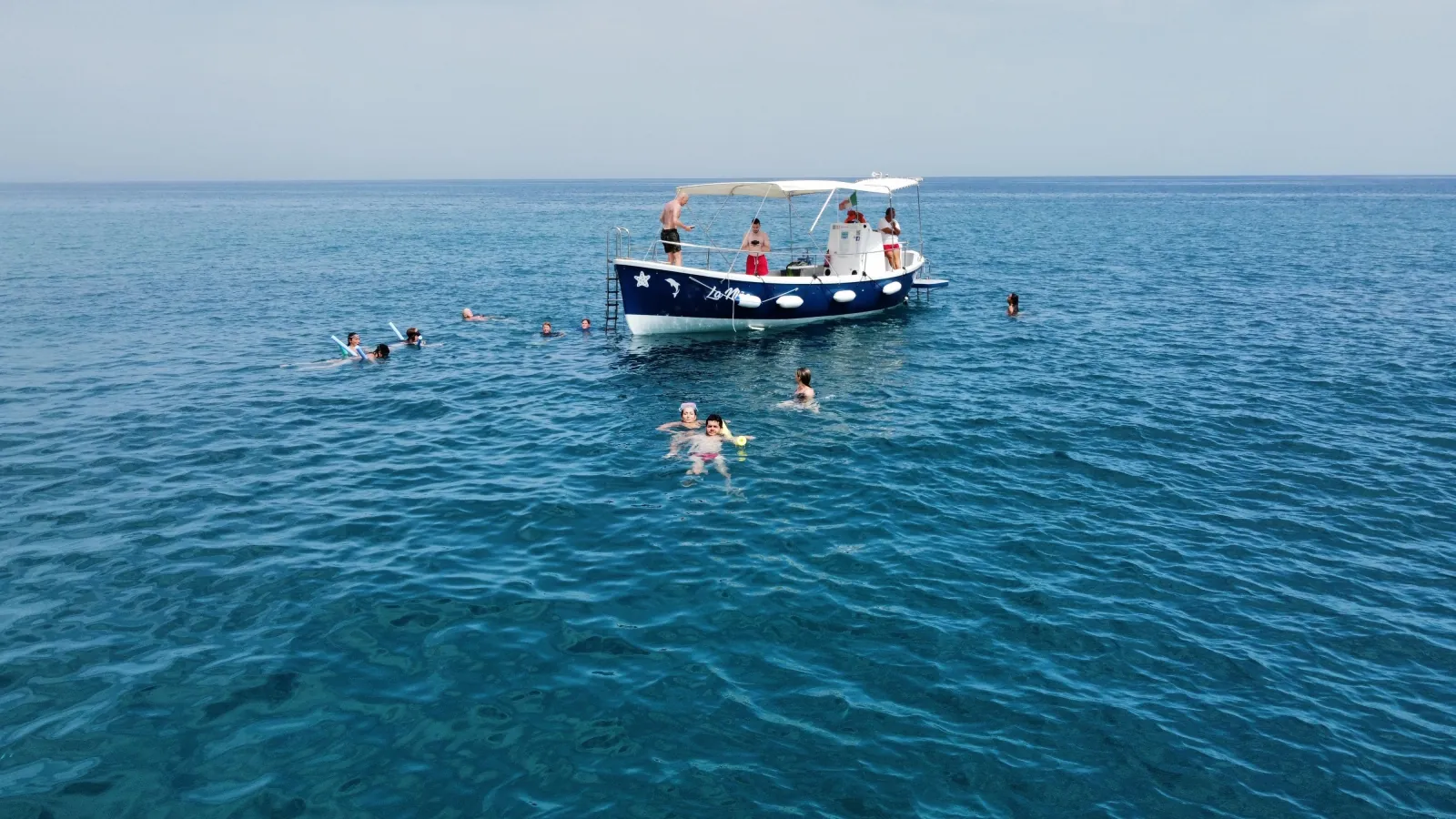 The boat lying off the coast with guests swimming in the flat evening sea