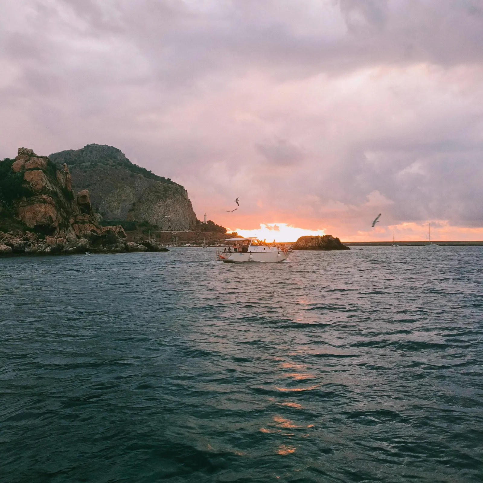 Sunset over the sea from the boat, with the headland in silhouette