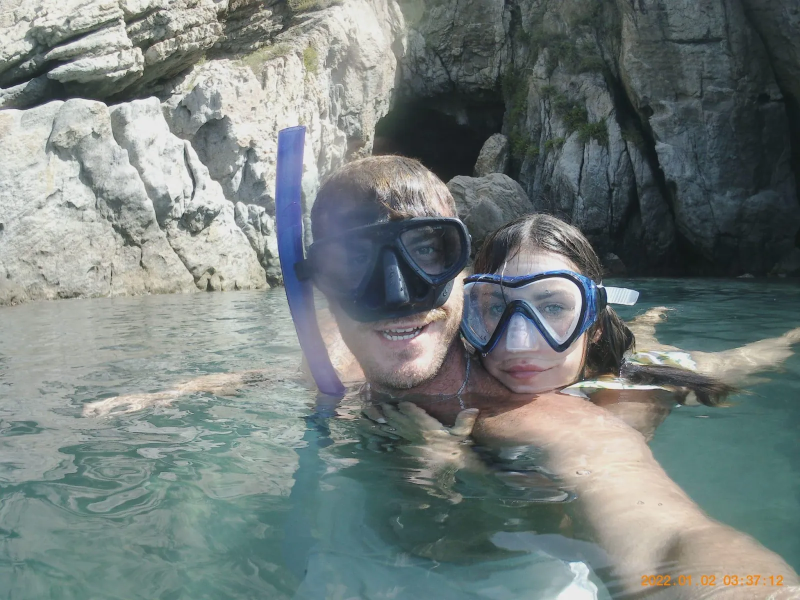 Two guests in snorkelling masks in the water at the mouth of a sea cave