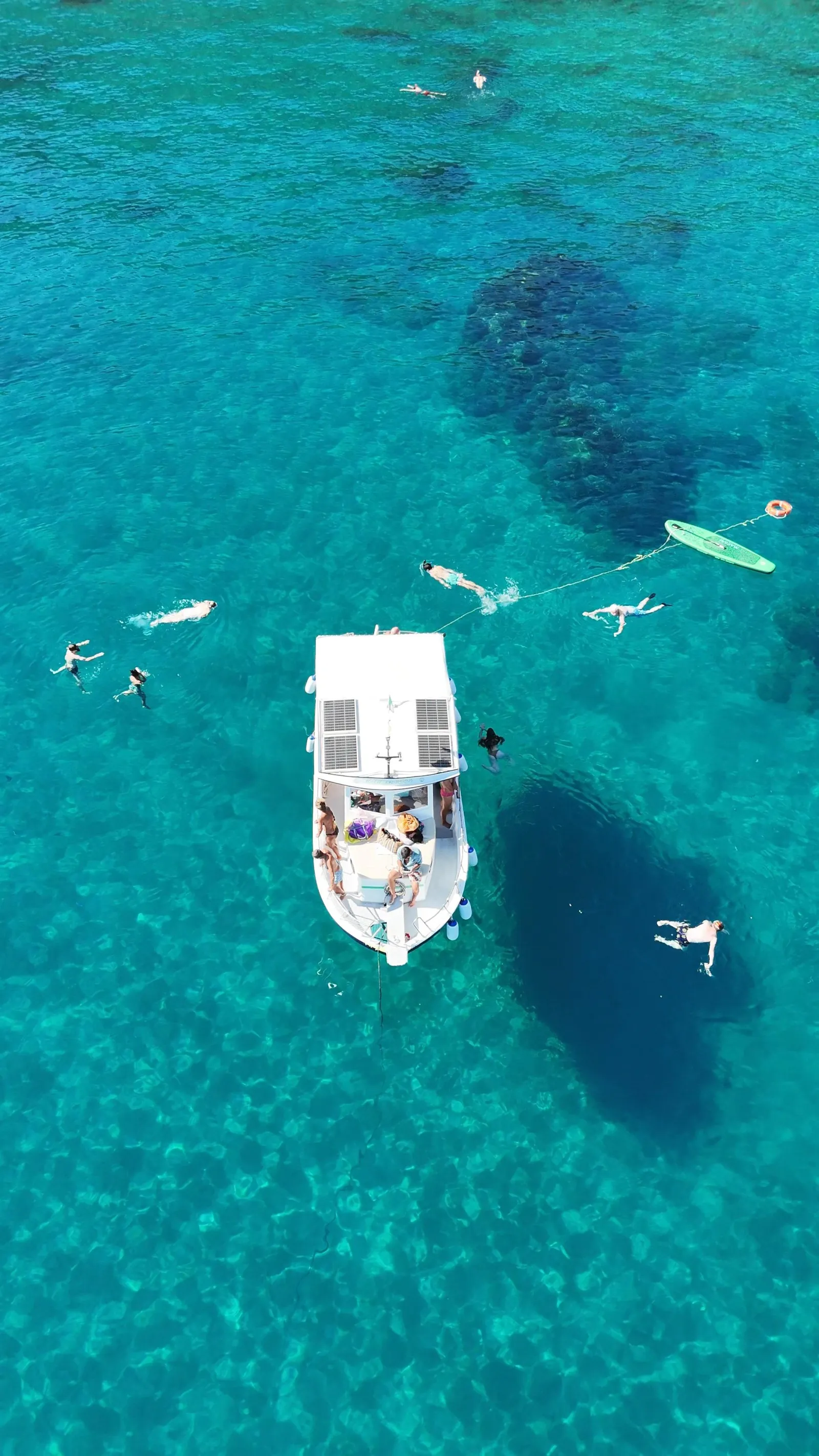 Aerial view of the boat anchored over clear turquoise water, with guests swimming and snorkelling alongside
