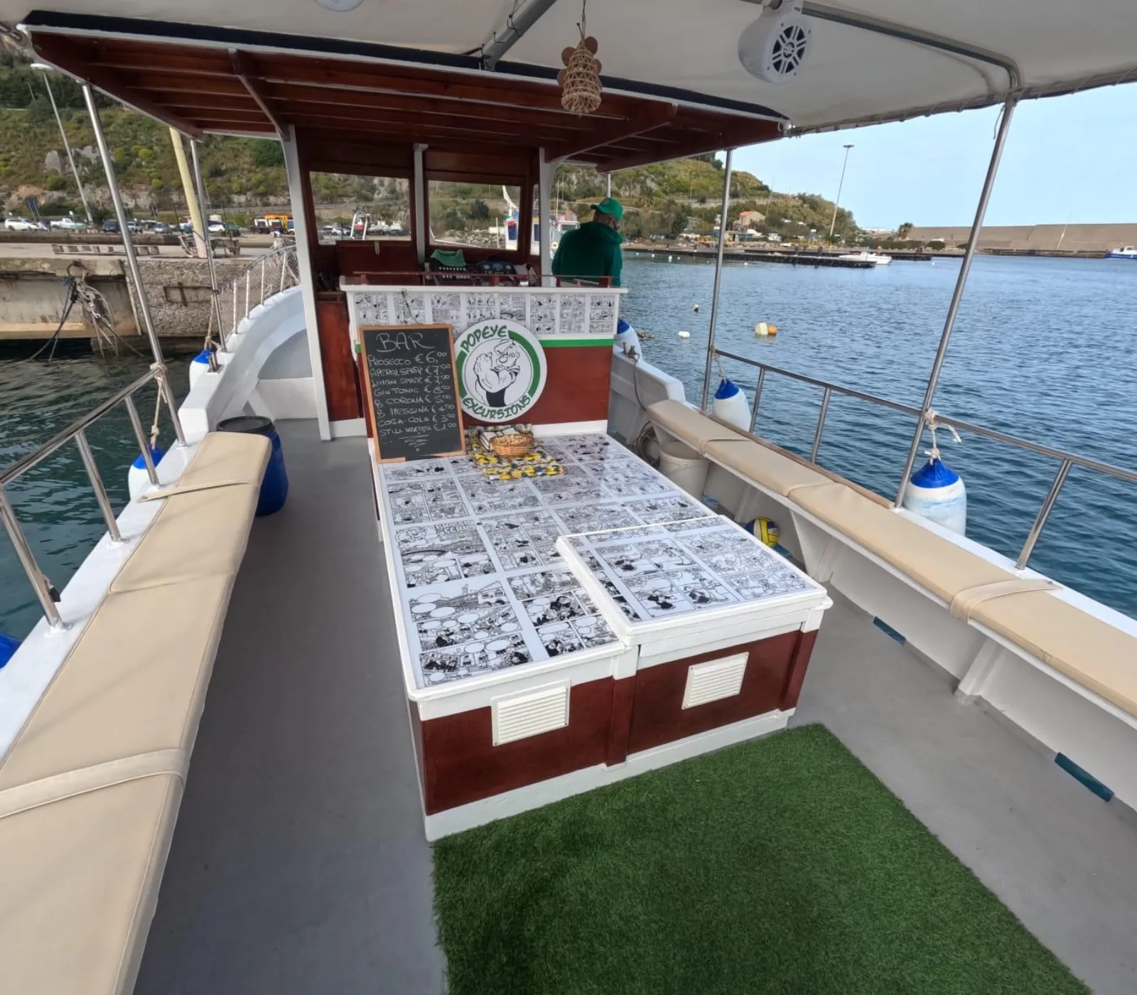 The boat's shaded deck, with cushioned bench seating along both sides, moored at Porto Presidiana