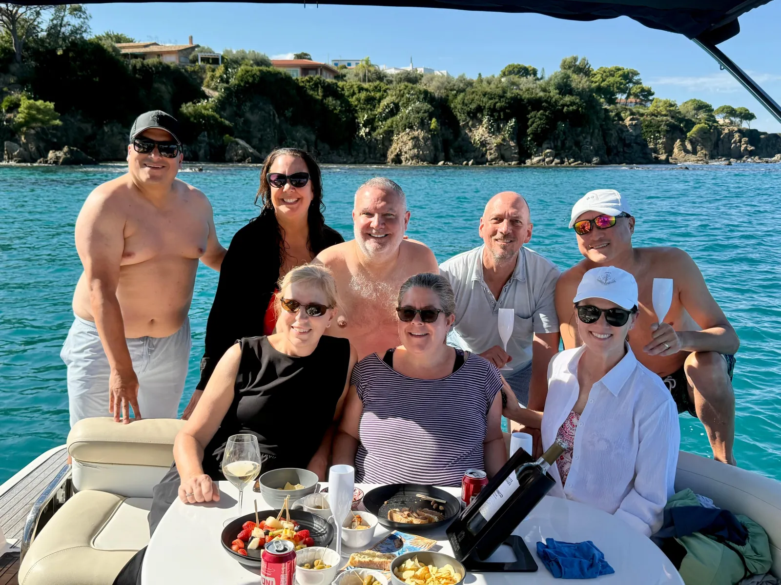 Guests gathered around the aperitivo table on deck, glasses in hand, at anchor below the cliffs
