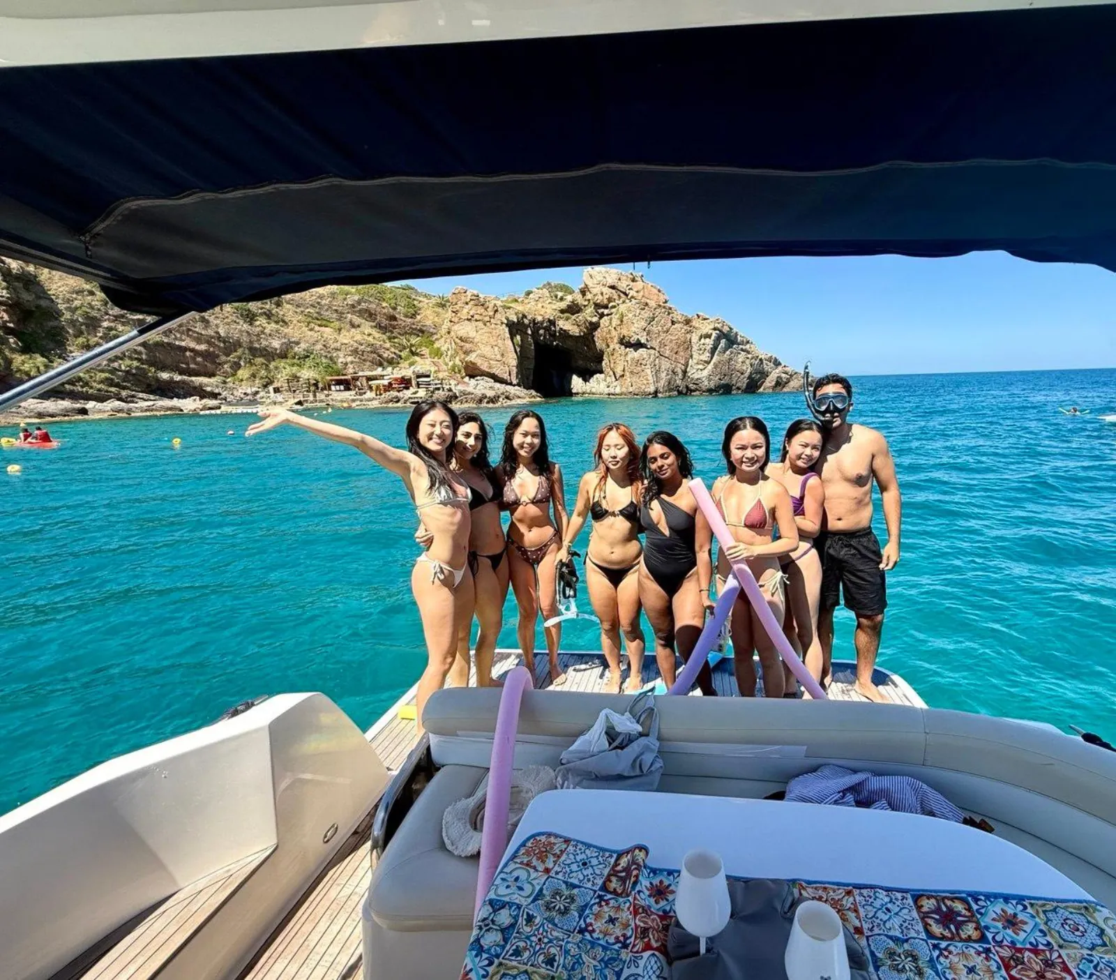 Guests standing along the bow at a swimming stop in a turquoise cove