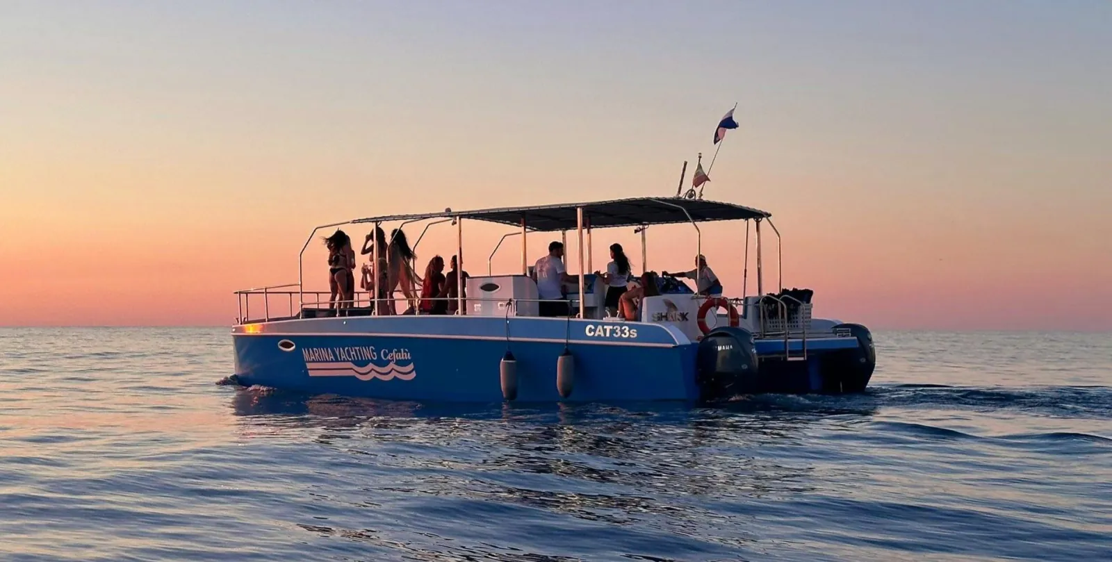 The catamaran under way at sunset, guests gathered under the canopy