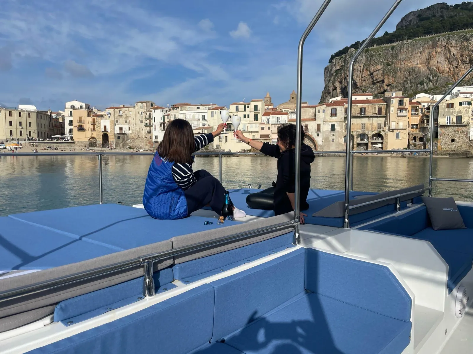 Two guests sitting on the catamaran's foredeck with the old town behind them