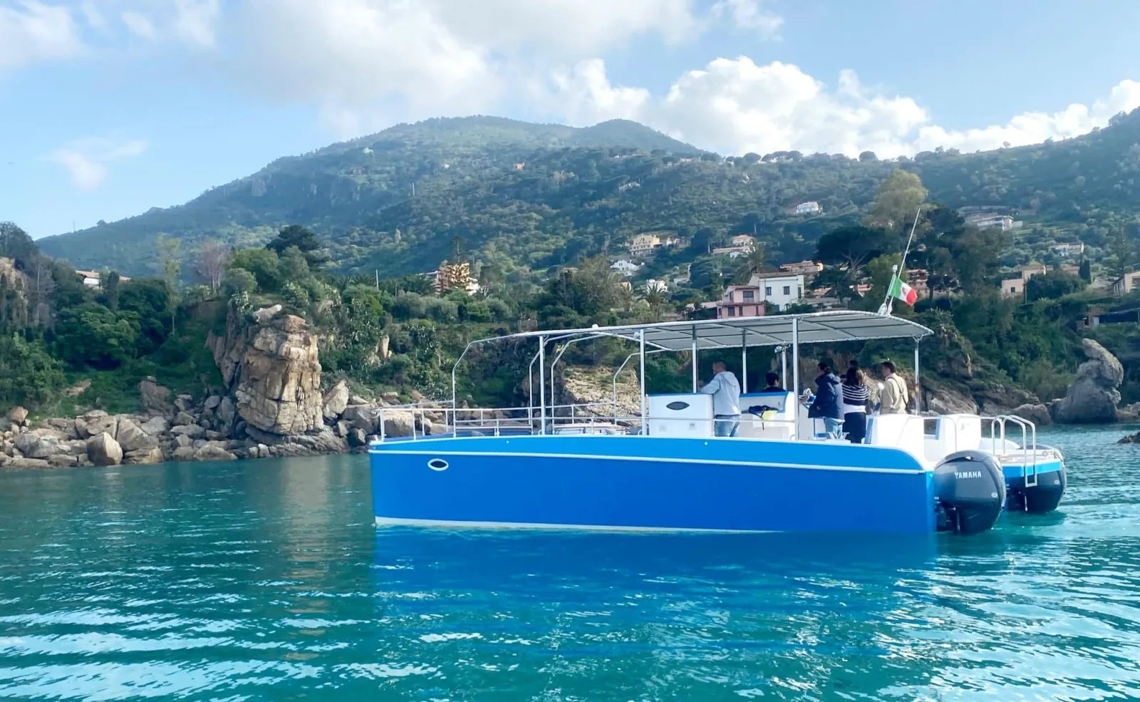 The catamaran at anchor in a turquoise cove with the green hills of the coast behind
